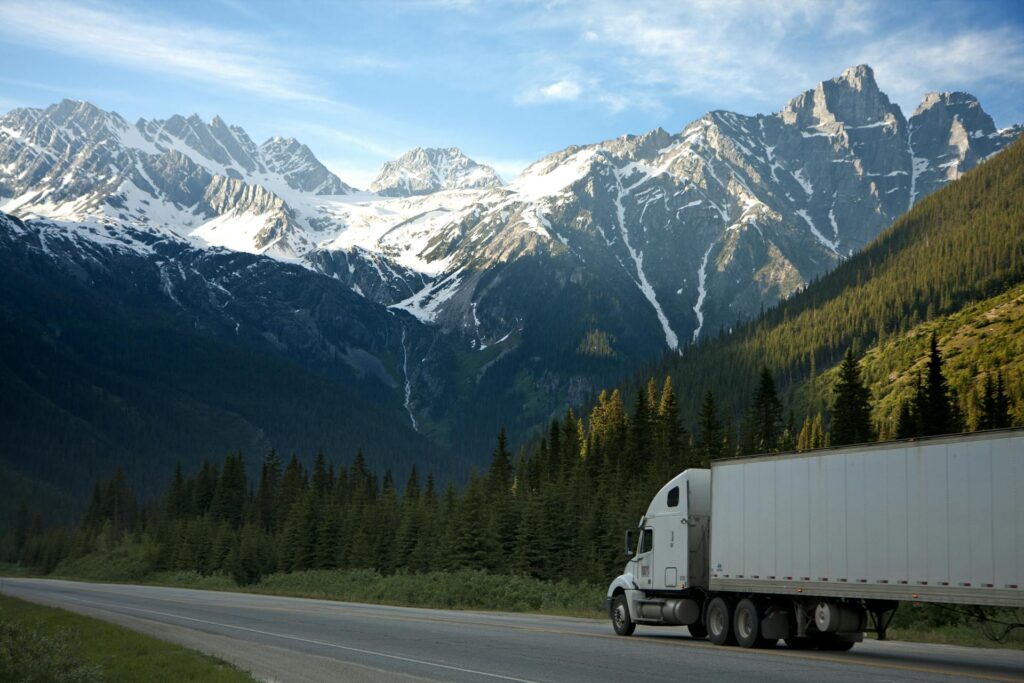 Semi truck on a highway through the forest with snowy mountains