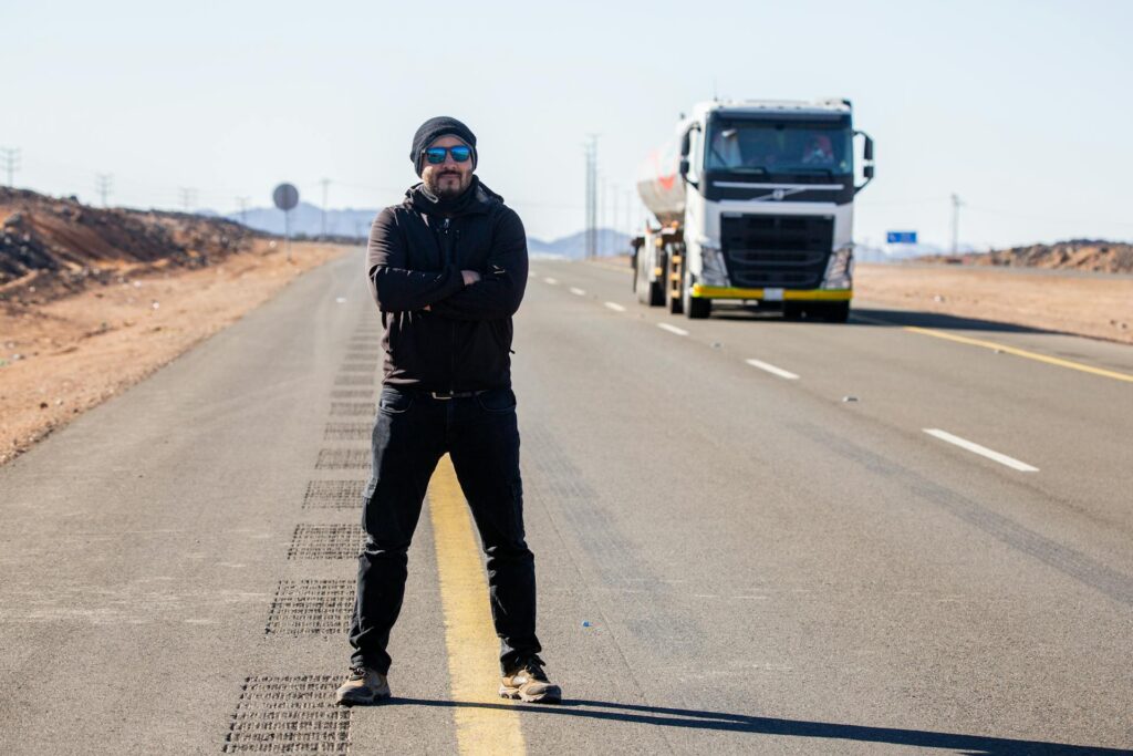 Truck driver wearing sunglasses standing on the side of the road in front of his rig